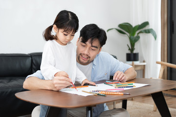 A pair of young Asian father and daughter are drawing in the living room