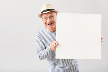 Portrait of elderly man with blank poster on grey background