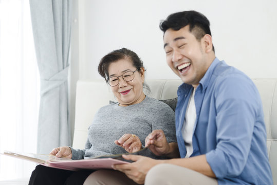 Asian man and his mother looking at photo album together while staying at home.