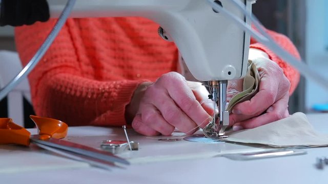 Hands of a seamstress making a protective mask on her face. Sewing machine needle seam on fabric. Self-employment in self-isolation.