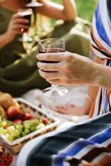Hand with a glass of red vine on picnic. close up. vertical photo
