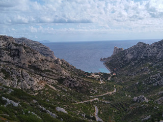 Mountains with green grass and grey rocks near the sea. Blue sky and white clouds.