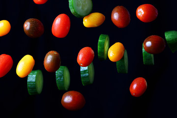 colored juicy tomatoes and sliced cucumber in a drop on a dark background