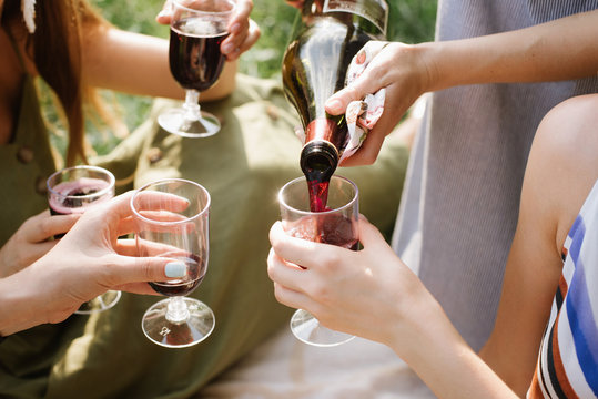 cropped image of girls or friends pouring red wine in glasses in park outdoor. close up