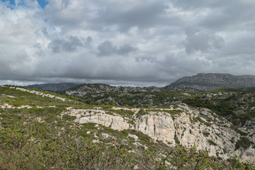Mountains with green grass and grey rocks near the sea. Blue sky and white clouds.