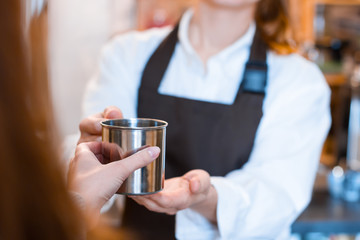 Closeup female hands are holding metal reusable cup of coffee. Woman  prepared, brewed espresso, americano, latte cappuccino in cafe. Barista is giving order to client. Take away, to go concept.