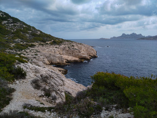 Mountains with green grass and grey rocks near the sea. Blue sky and white clouds.