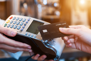 Closeup of female hands are holding terminal in cafe, restaurant, shop. Seller, waiter, barista is accepting payment. Female customer is paying order with credit card. Cashless money concept.