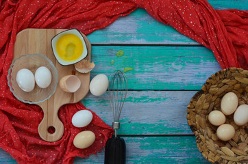 Background Easter holiday raw eggs on a wooden cutting Board, whisk, eggshell, yolk and handkerchief on a wooden blue table