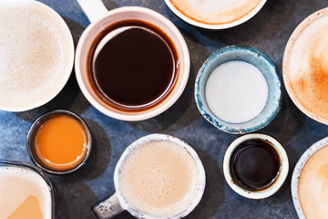 Closeup small and big colorful clay cups with latte, cappuccino, americano, espresso, mocha on grey table in cafe, restaurant. Aromatic morning coffee for breakfast. Hot drinks, beverages concept.