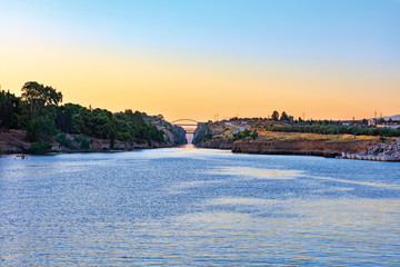 The Corinth Canal in the morning summer day illuminates the bright rising sun of Greece.