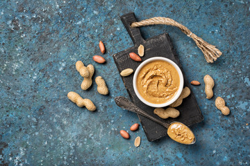 Tasty peanut paste in white bowl and vintage spoon with raw nuts