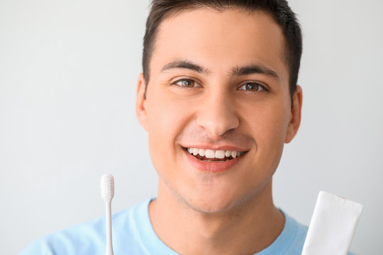 Handsome man with tooth brush and paste on light background