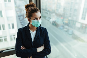 Businesswoman with face mask standing with arms crossed by the window.