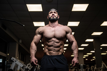 Fototapeta na wymiar perfect physique body of young bearded athlete with strong muscles in dark fitness club gym during heavy workout training with weights