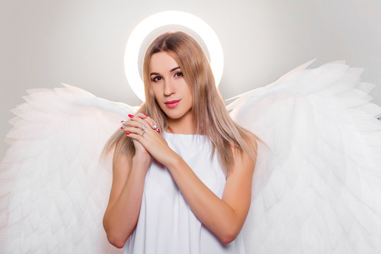 Angel in a white dress with large white wings behind his back and a halo above his head. Portrait of an attractive girl in a fantasy look.