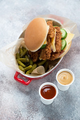Serving bowl with double chicken strips burger, pickles and dips, studio shot on a beige stone background