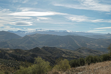 Mountains with snow on the top. Green hills under the blue sky with white clouds.