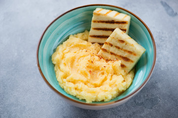 Turquoise bowl with polenta and roasted cheese, horizontal shot on a light-blue stone background