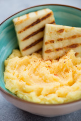 Closeup of polenta with fried cheese in a turquoise bowl, vertical shot, selective focus