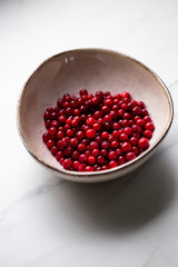 lingonberry berries in white bowl on marble table