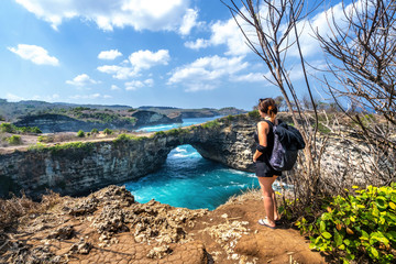Fototapeta na wymiar Travel people with backpack and in shorts on the ocean, cliffs and tropical beach background. Angel's Billabong beach, Nusa Penida, Indonesia. 