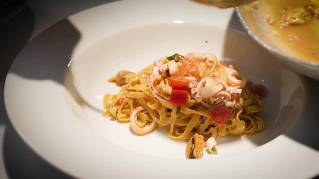 Cuoco versa nel piatto delle pasta fresca italiana con condimento di mare