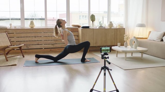 Attractive Caucasian female recording making live stream or vlog about doing yoga at home. Stay home, quarantine workout. Shot on ARRI Alexa Mini with Cooke S4 lenses
