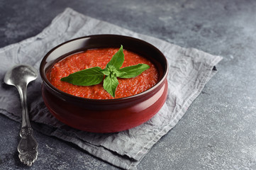 Gazpacho cold summer vegetarian tomato soup with basil in a bowl on a towel. Vintage spoon nest to bowl. Grey stone background. Copy space.