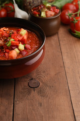 Cold summer gazpacho soup in bowl with ingredients on wood board desk. Copy space on brown wooden background. Recipe of tomato summer soup. Tomato, pepper, garlic, cucumber, greens. Menu.