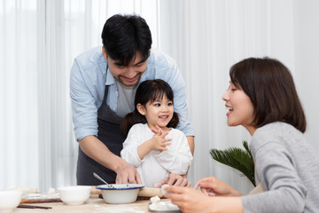 Young Asian mom and dad making dumplings with daughter