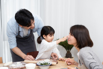 Young Asian mom and dad making dumplings with daughter