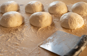 Stay at home for coronavirus covid-19 lockdown concept: make pizza at home. Backlit low angle view of leavened dough portions ready to bake on a light wooden work table dusted with flour