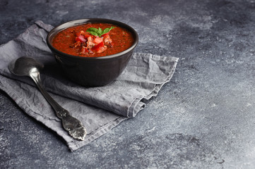 Bowl of homemade gazpacho soup. Vintage spoon on grey towel next to bowl with cold spicy tomato soup. Copy space on textured grey stone desk. 
