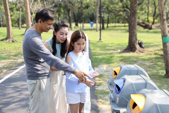 Group of happy asian family in the park, parents teaching children to throw empty plastic bottle into the garbage with smiling face.