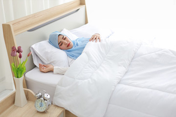 Obraz na płótnie Canvas Oversleeping asian muslim woman wearing white sleepwear lying on bed with happiness.Top view portrait young cute girl sleeping in bedroom with happy and beauty face. Lifestyle concept