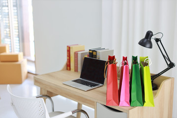 Shopping bags on wooden working table with computer black blank screen and books in room house indoor. Free space for your advertisement