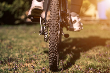 Bike at the summer sunset on the grass in the city park. Cycle closeup wheel on blurred summer background. Cycling down the street to work at summer sunset. Bicycle and ecology lifestyle concept.