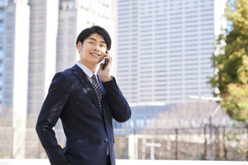 ビルを背景に電話する日本人男性ビジネスマン