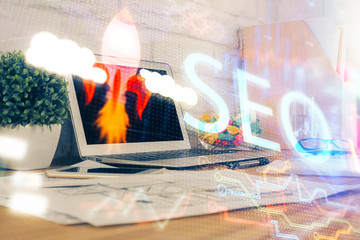 Double exposure of table with computer and seo drawing hologram. Search optimization concept.