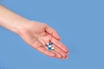 hand holds out the pills . blue background.
