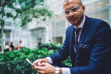 Calm adult businessman using smartphone on street in daytime