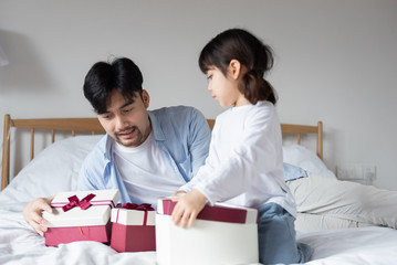 Young Asian dad is unpacking gifts on bed with daughter