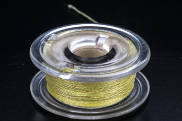 Close up of a sewing machine bobbin with yellow thread on a black background.