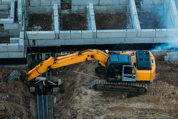 aerial view on a yellow excavator working at a construction site next to the foundation of a...