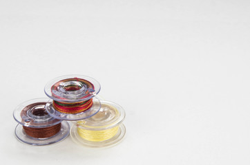 Close up of a groups of three sewing machine bobbins with colourful thread on a white background.