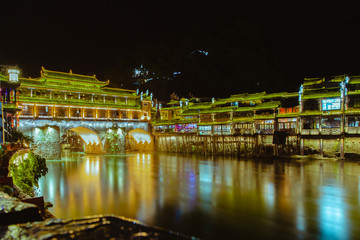 View of illuminated at night riverside houses and bridge in ancient town of Fenghuang known as Phoenix, China.