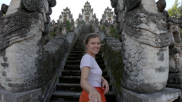 Follow me to Asia, young smiling woman leading boyfriend to beautiful old stairs with dragons at balinese temple, wearing traditional orange sarong and purple t-shirt, Lempuyang Temple, Bali,Indonesia