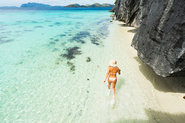 Fototapeta na wymiar Woman in bikini and hat running on the beach with rock. Coron, Philippines. Legs in motion blur.
