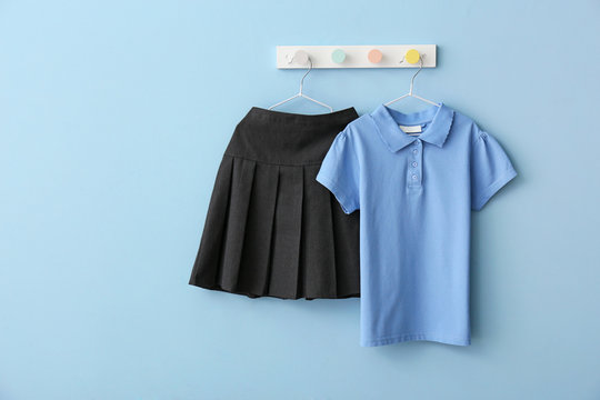Stylish school uniform hanging on color wall